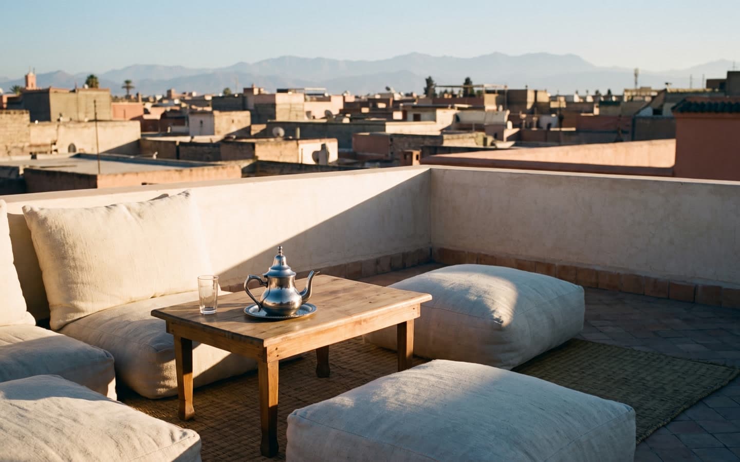A rooftop terrace in the Marrakech medina at the end of the workday, the Atlas range faint on the horizon